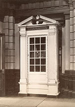 Tall, architectural case with column-like details, carved moulding, and window.